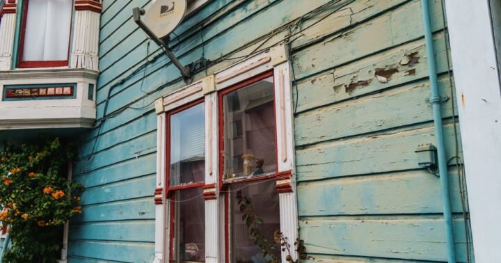 Sell house as-is in Texas – older wooden house with worn teal paint and aged window trim