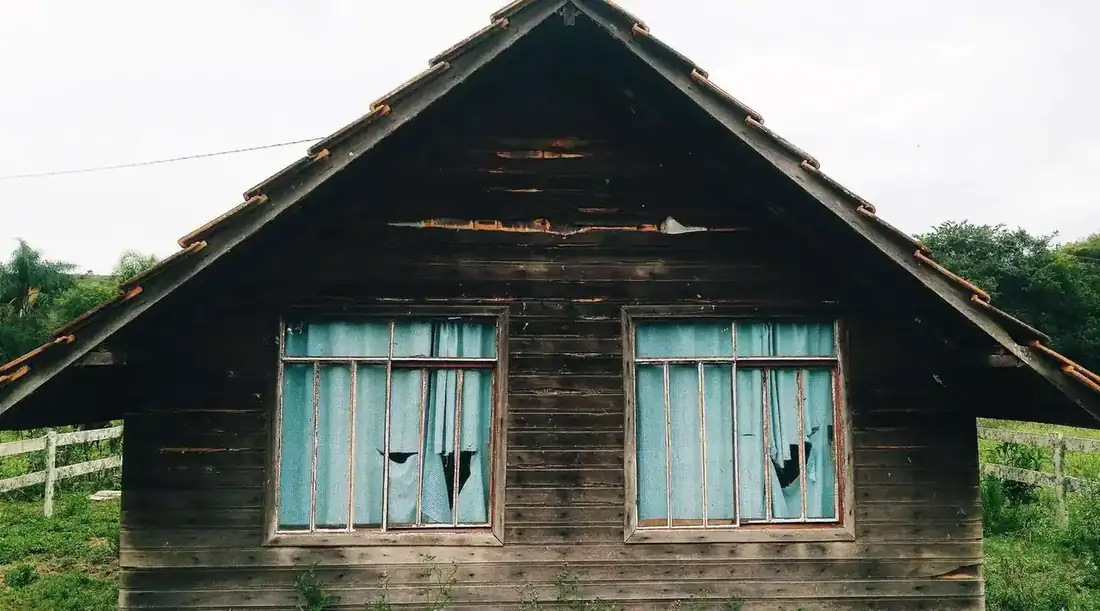 Sell damaged house Texas – weathered wooden house with broken window screens